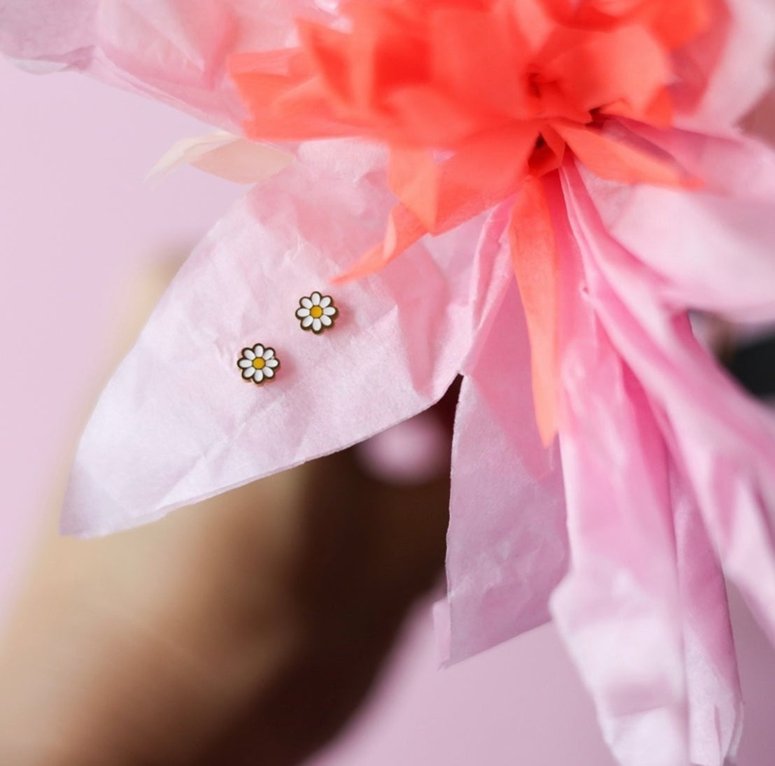 Flower-shaped earrings on a pink fabric background