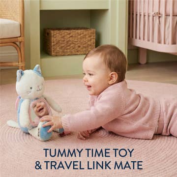 Baby playing with a plush toy on a pink blanket in a nursery.