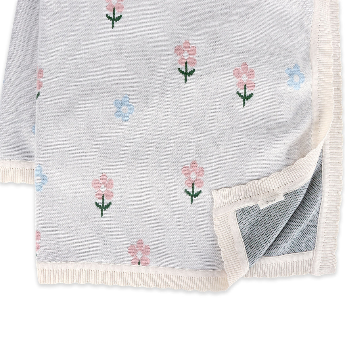 A close-up of a soft knit blanket or throw in a very light gray color, decorated with a delicate pattern of small pink and blue flowers with green stems. The blanket features cream-colored ribbed borders and is shown folded with its underside visible.