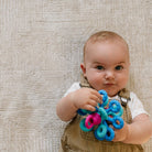 Baby holding a colorful toy against a textured beige background