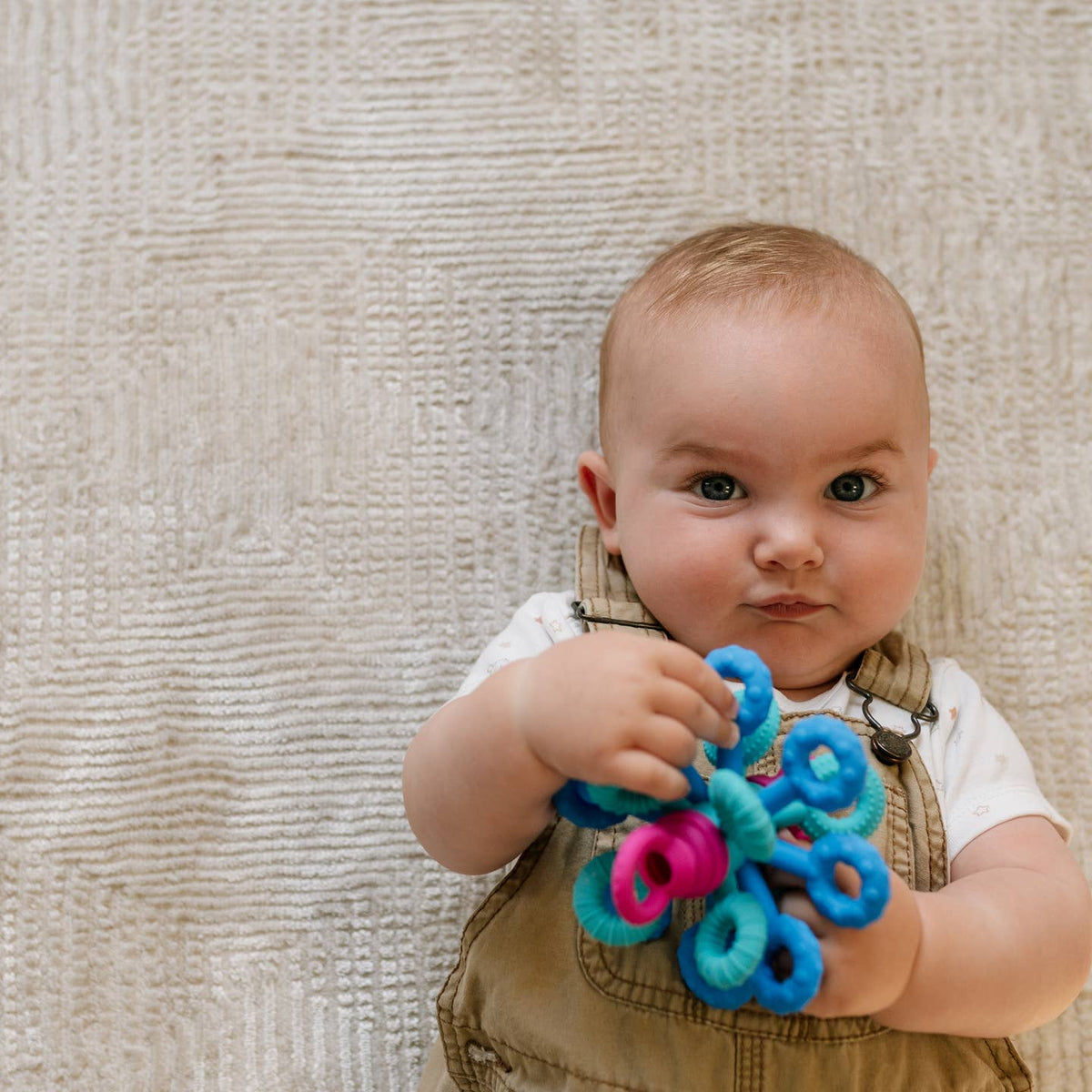 Baby holding a colorful toy against a textured beige background