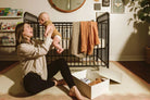 Woman holding a baby in a nursery with a crib and toys on the floor.