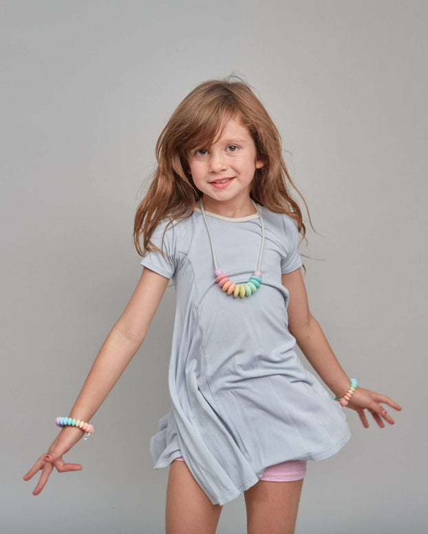 Young girl wearing a light gray dress with colorful necklace against a gray background