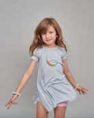 Young girl wearing a light gray dress with colorful necklace against a gray background