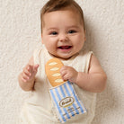 Baby holding a toy loaf of bread and package on a soft surface