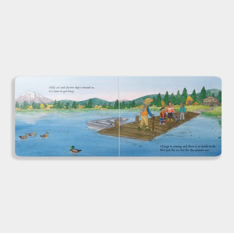 An open spread of the board book When Fall Comes showing an illustration of a lake landscape at sunset, with a person in a small boat and a deer standing on the shore under autumn trees.