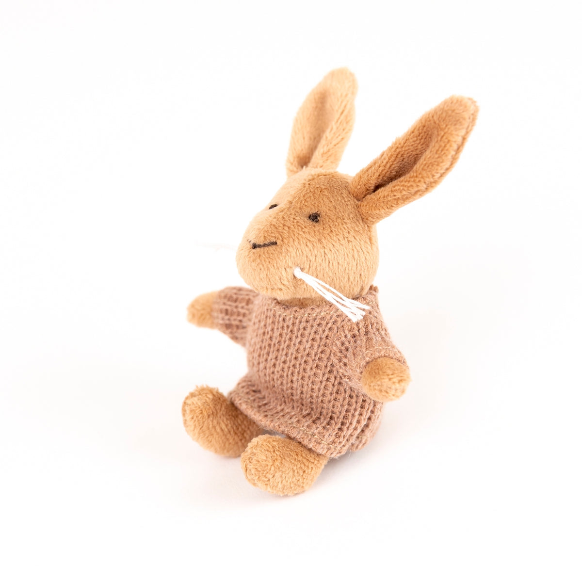 A small plush rabbit toy in warm tan and light brown, wearing a knitted brown sweater and white whiskers, photographed on a clean white background.
