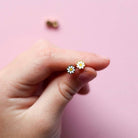 Hand holding a pair of daisy-shaped earrings against a pink background
