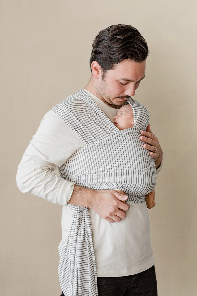 Man holding a baby in a textured wrap against a beige background