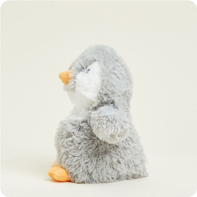 Side view of the Gray Penguin by Warmies plush toy showing its soft gray and white body, orange beak and feet, and one outspread flipper against a light background.