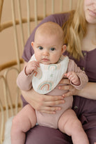 Baby wearing a rainbow bib held by a person in a soft, indoor setting