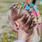 Child with braided hair adorned with colorful butterfly hair clips in a natural setting.