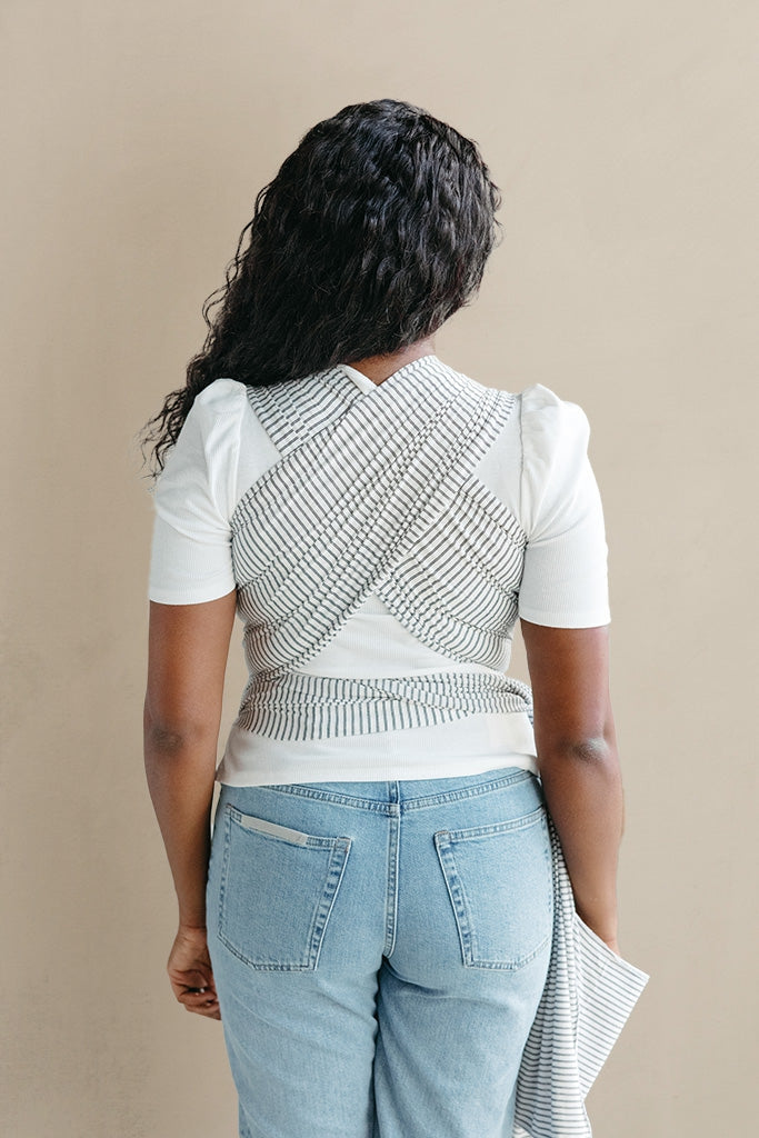 Person wearing a white t-shirt with a geometric patterned vest over it, standing against a beige background.