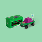 Toy car with purple roof and green body next to its packaging on a light green background