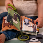Child holding a soft book with animal illustrations and green handle.