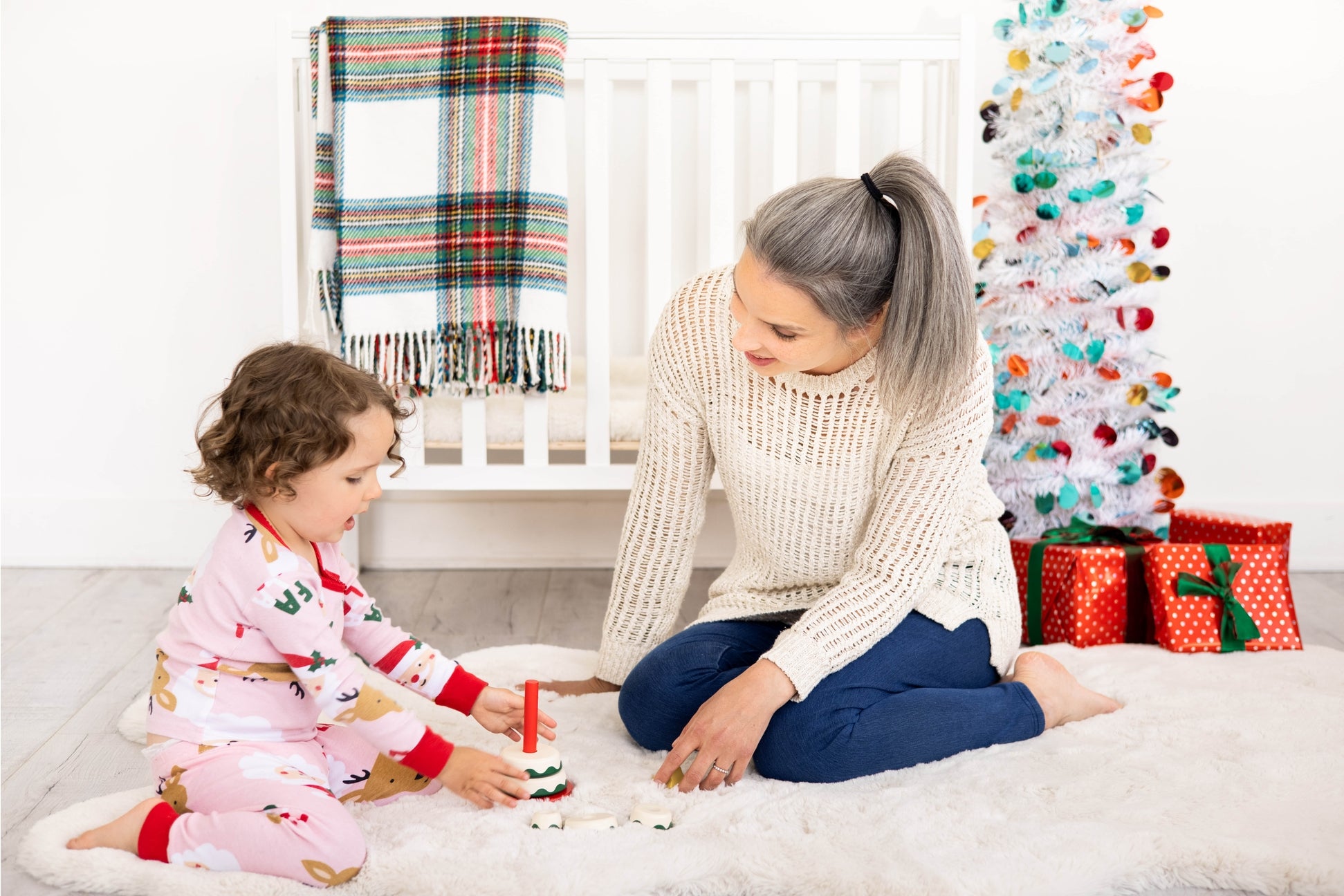 Woman and child playing on a white rug with Christmas decorations in the background