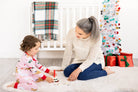 Woman and child playing on a white rug with Christmas decorations in the background