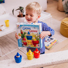 Child holding a 'Gnome' puzzle game box with colorful gnome figurines on a wooden floor.
