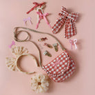 Collection of children's accessories including a checkered purse, headbands, and hair clips on a pink background.