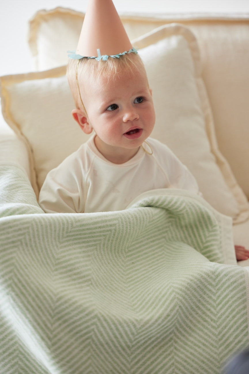 Child sitting on a couch wearing a hat with blanket.