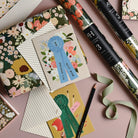 Decorative ribbons, cards, and stationery items on a pink surface