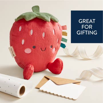Plush strawberry toy with ribbons and gift wrap on a light background