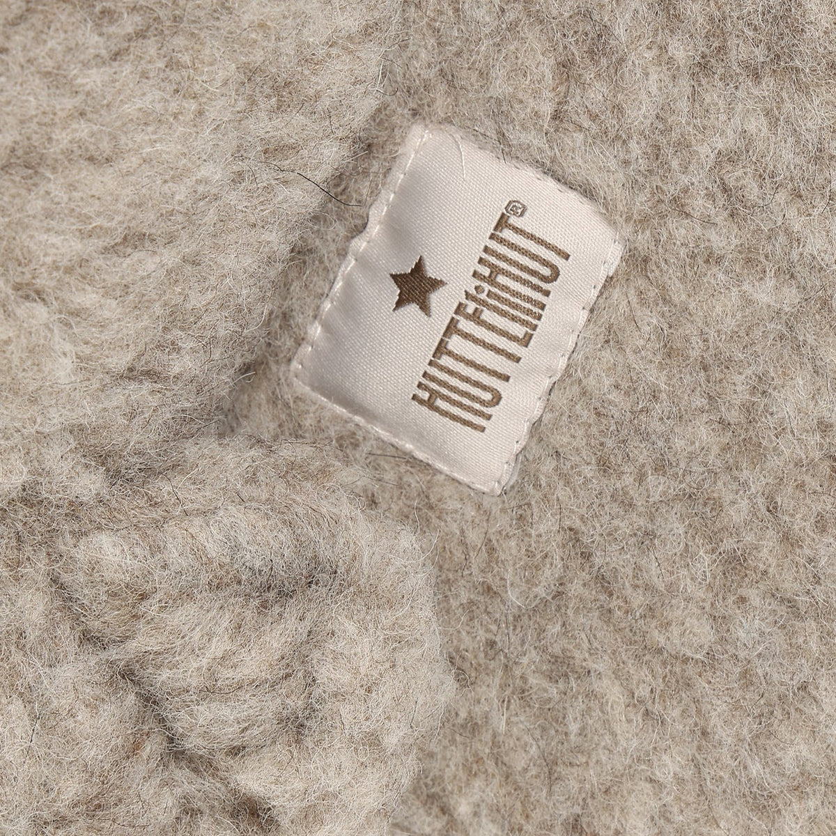 Close-up of the brand label on the camel melange wool teddy balaclava by Huttelihut.