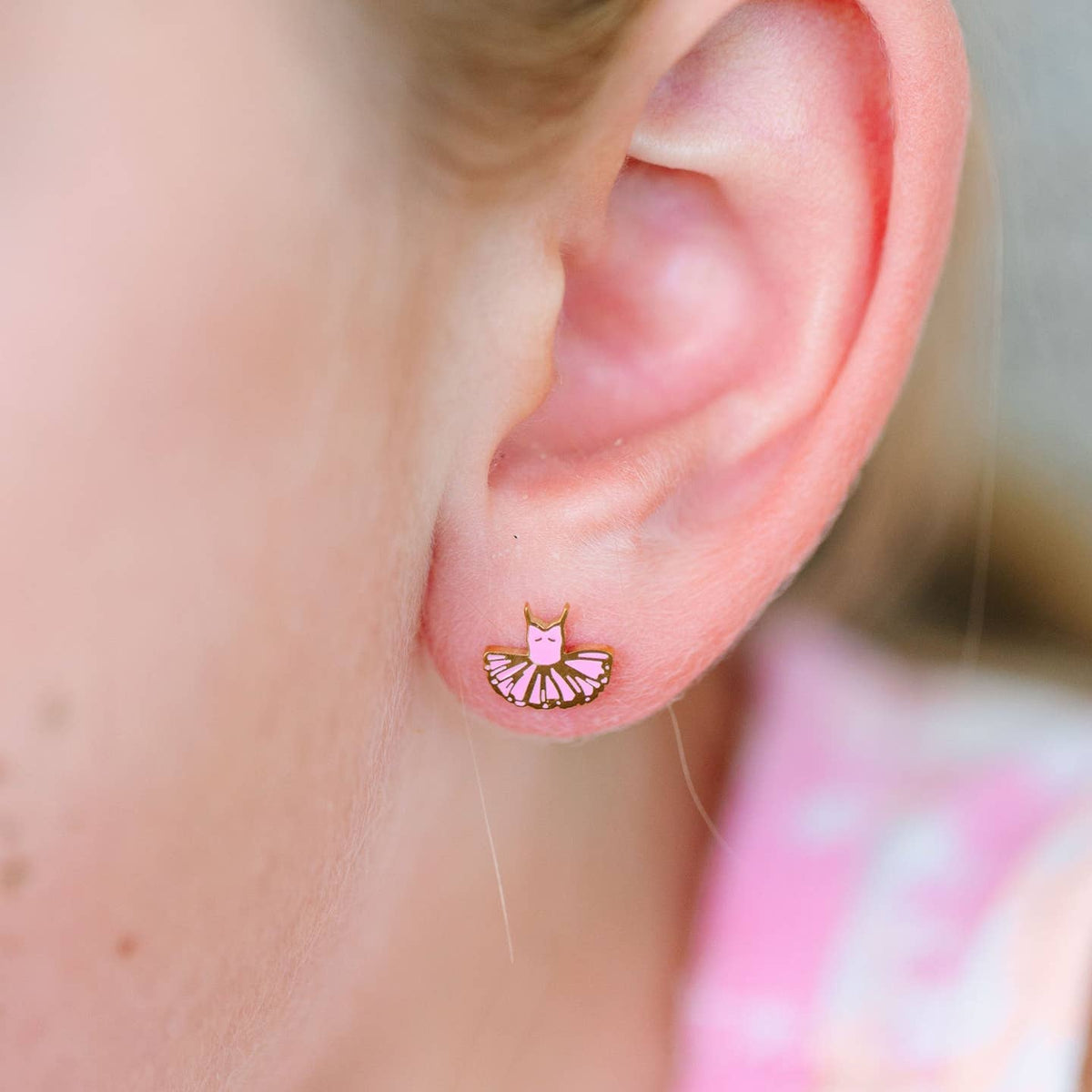 Close-up of an ear wearing a pink ballerina-themed earring with a blurred background