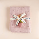 Pink knitted blanket with a wooden spoon and pink strawberry toy, tied with a ribbon on a beige background.
