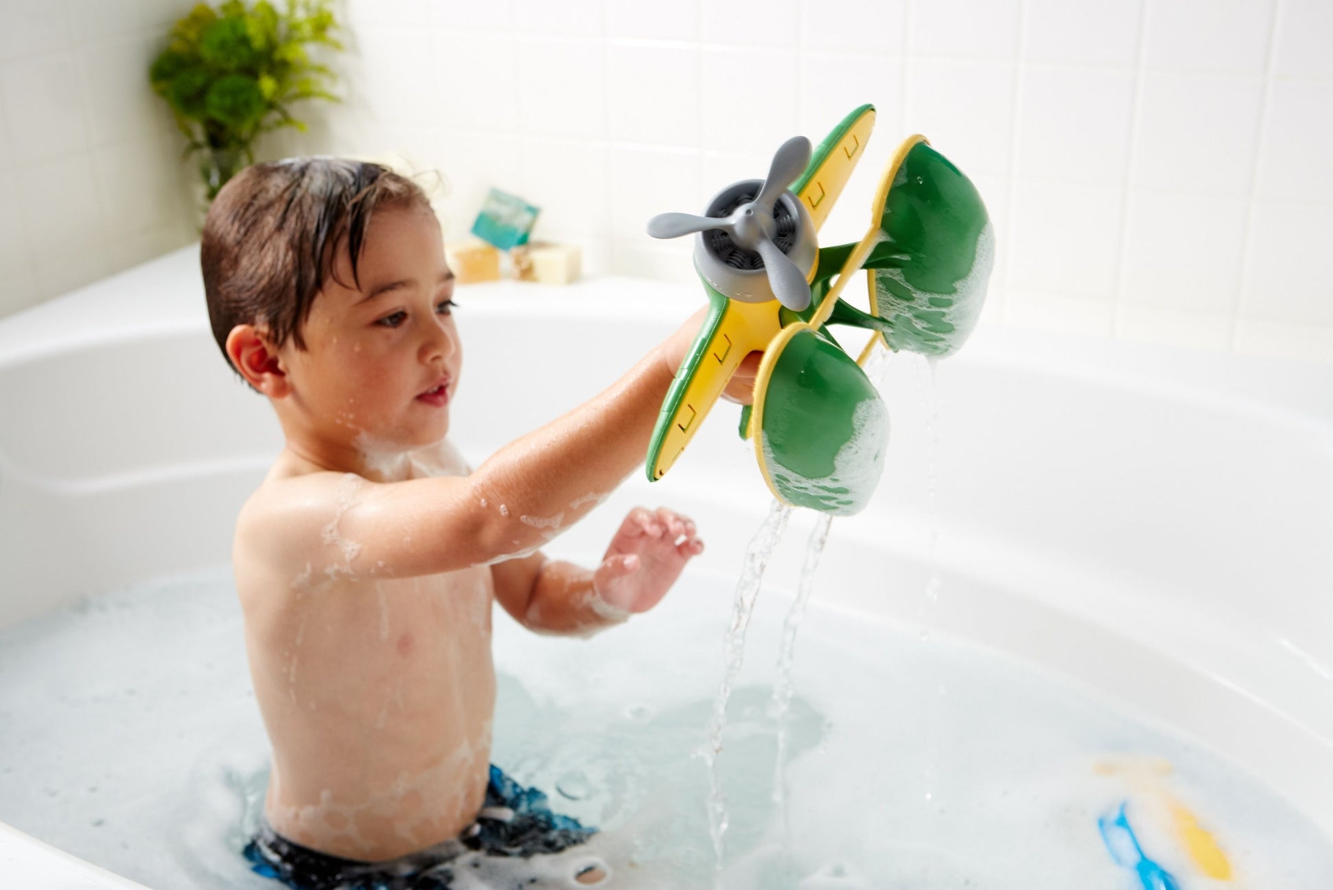 Child playing with a toy airplane in a bathtub