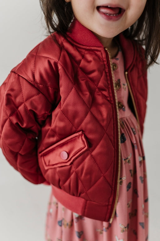 Child wearing a red jacket over a pink dress.