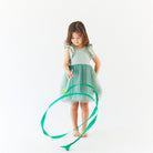 Young girl in a light blue dress with a green ribbon on a white background