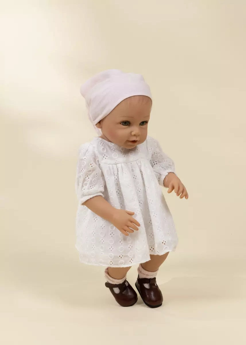 Baby doll wearing a white lace dress and bonnet on a beige background