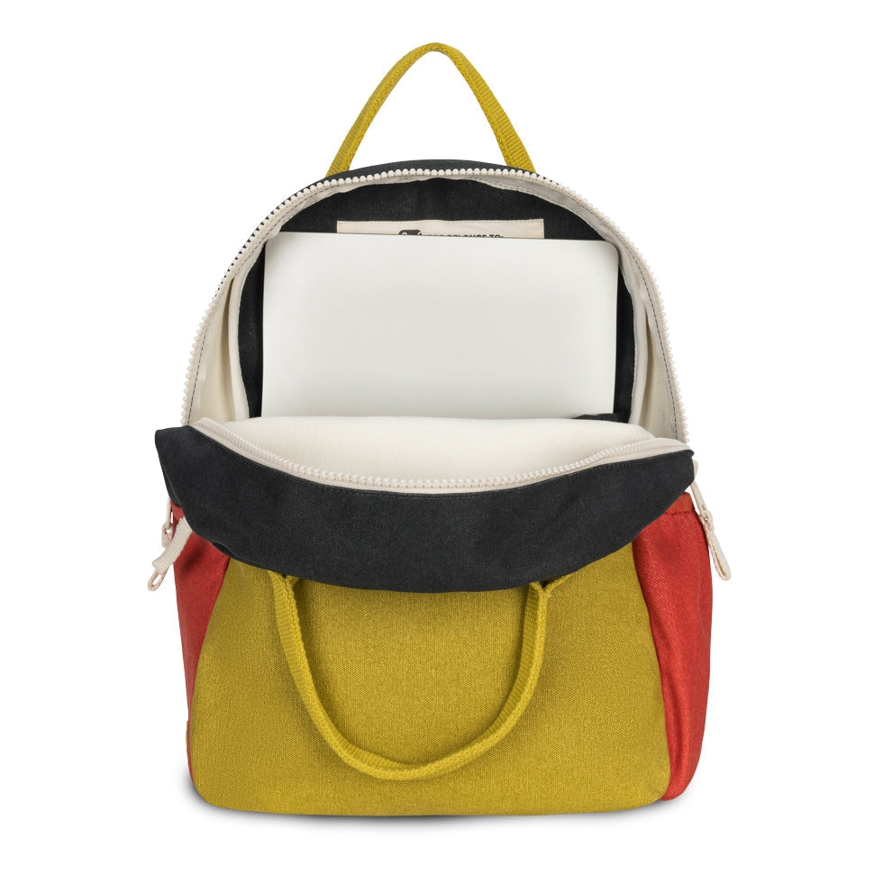 A color-blocked backpack shown open, featuring a mustard yellow body, a black suede-like front flap, red side panels, and off-white interior lining with a white laptop insert, photographed on a white background.
