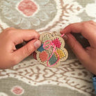Handmade cross-stitched heart ornament held by a person on a patterned fabric background