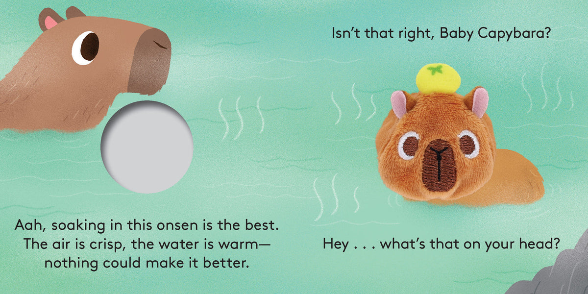 An illustrated spread from "Baby Capybara - Finger Puppet Book" showing an adult capybara and a plush baby capybara finger puppet relaxing in a hot spring with yuzu fruit, alongside a finger hole and text that reads "Aah, soaking in this onsen is the best. The air is crisp, the water is warm—nothing could make it better.", "Hey... what's that on your head?", and "Isn't that right, Baby Capybara?".