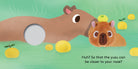 An illustrated spread from "Baby Capybara - Finger Puppet Book" showing an adult capybara and a plush baby capybara finger puppet relaxing in a hot spring with yuzu fruit, alongside a finger hole and text that reads "Huh? So that the yuzu can be closer to your nose?".