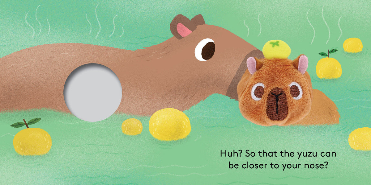 An illustrated spread from "Baby Capybara - Finger Puppet Book" showing an adult capybara and a plush baby capybara finger puppet relaxing in a hot spring with yuzu fruit, alongside a finger hole and text that reads "Huh? So that the yuzu can be closer to your nose?".