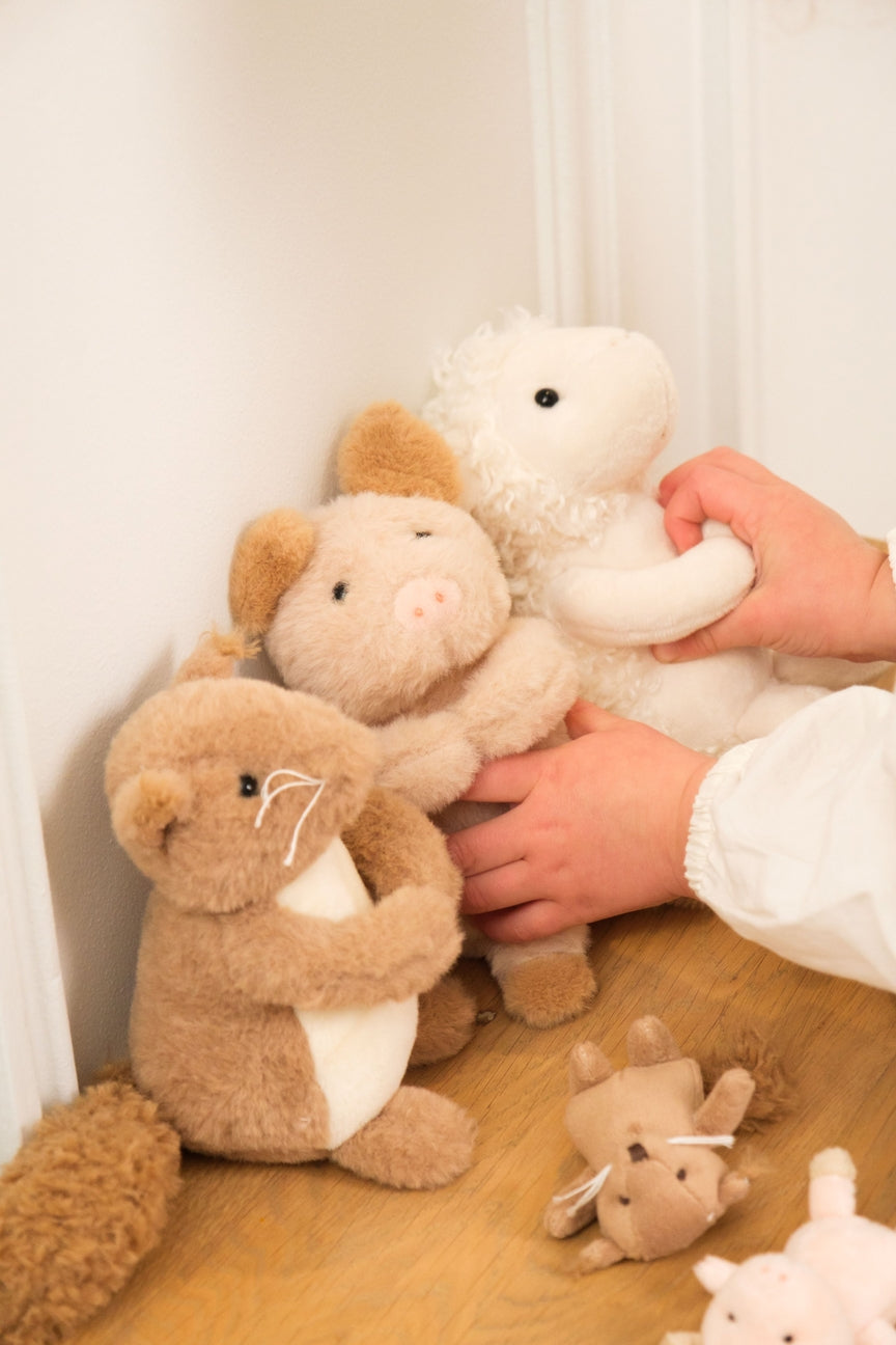 Collection of plush toys on a wooden surface with a person's hand interacting with them.