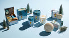 Collection of candles and packaging on a light blue background with decorative trees.
