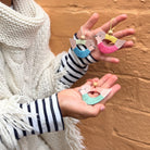 Hands holding colorful bird-shaped keychains against a wooden background