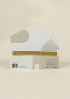 A packaged decorative item in a white house-shaped box with a gold glitter horizontal band across the middle, photographed against a plain warm beige background.