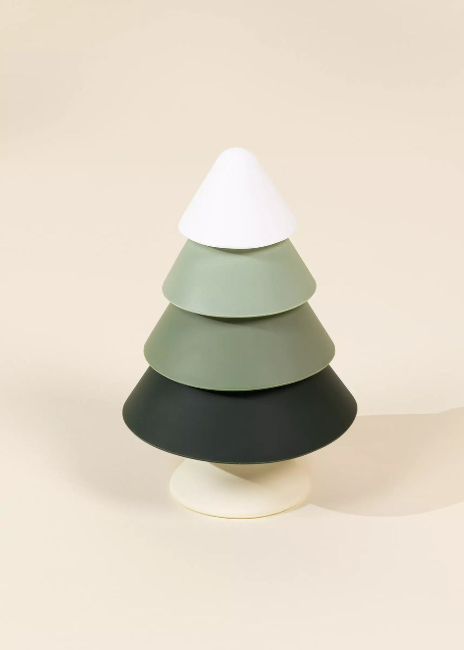 A minimalist, tiered Christmas tree sculpture made of matte-finish geometric discs in white, sage green, and charcoal black, set against a solid warm beige background.