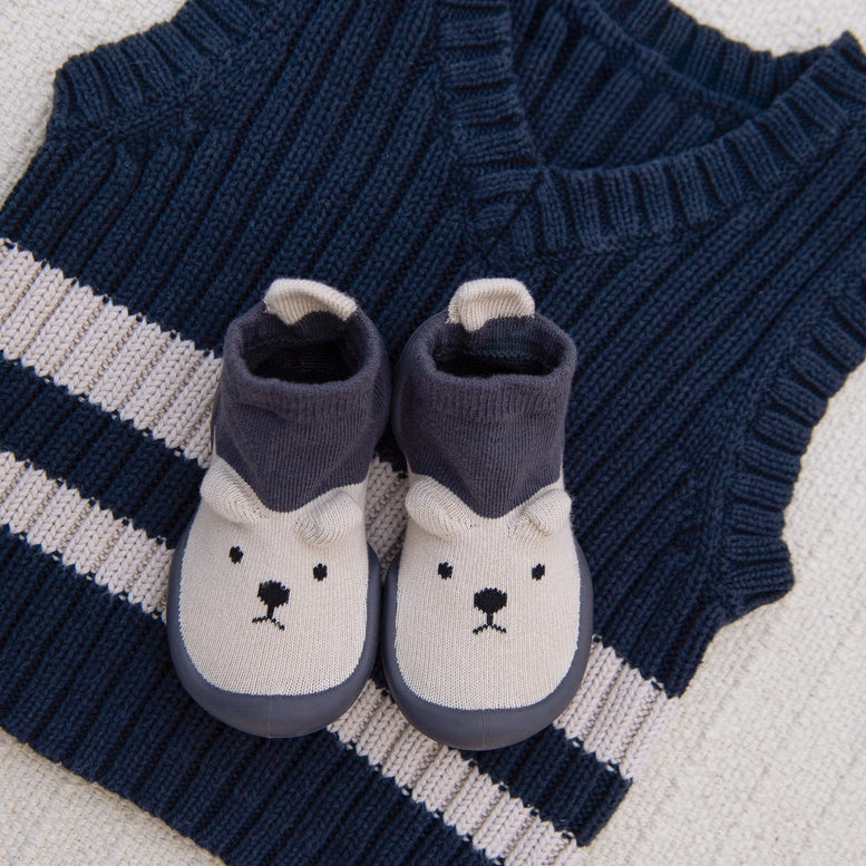 A pair of baby booties with a polar bear face design, styled on top of a navy blue and white striped knit sweater.