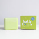 A pale yellow-green bath bomb bar standing next to its lime green packaging box on a white surface against a light gray background. The box is labeled 'bath bomb cosmic cooler' and features a blue 'Sugared Treats' logo.