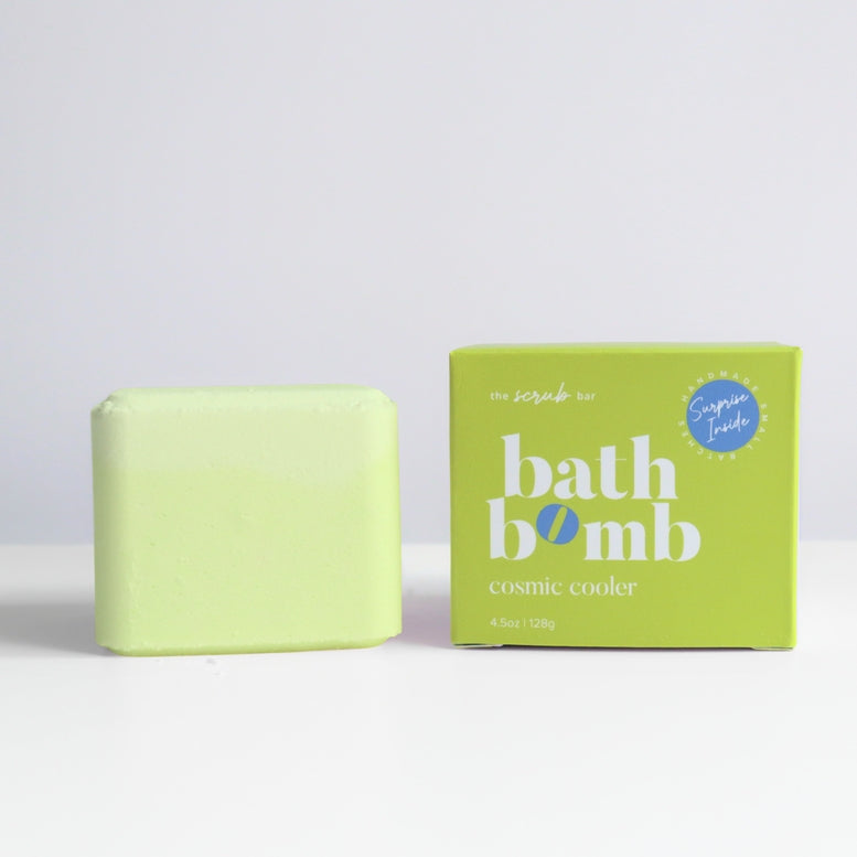 A pale yellow-green bath bomb bar standing next to its lime green packaging box on a white surface against a light gray background. The box is labeled 'bath bomb cosmic cooler' and features a blue 'Sugared Treats' logo.