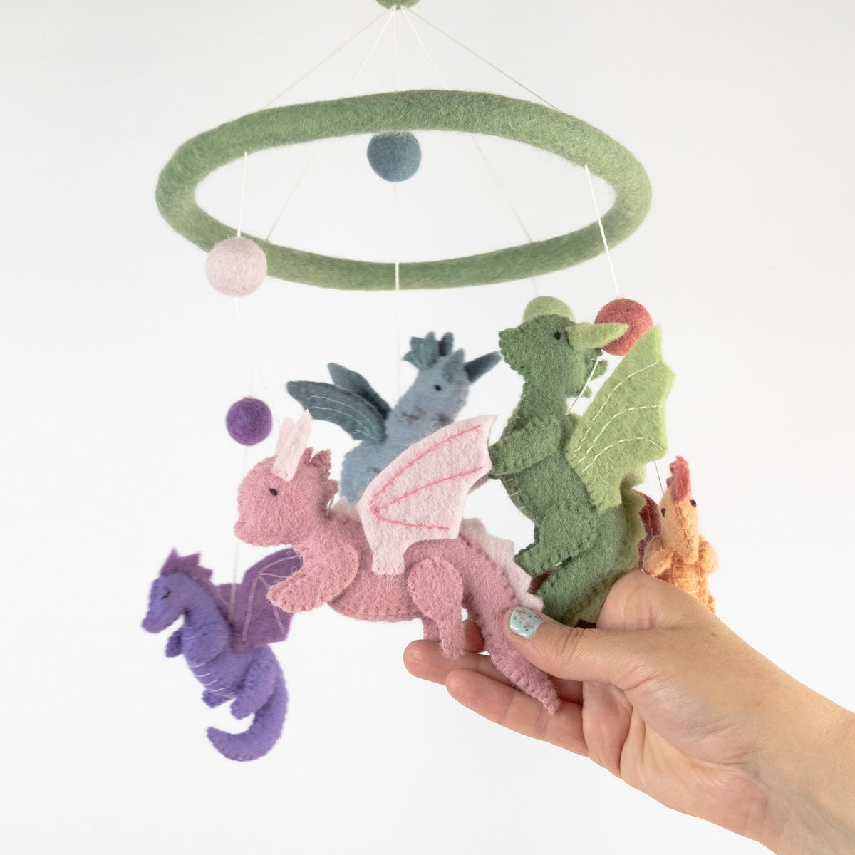 Plush dragon toys hanging from a mobile with a hand holding one of them against a white background.