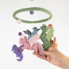 Plush dragon toys hanging from a mobile with a hand holding one of them against a white background.