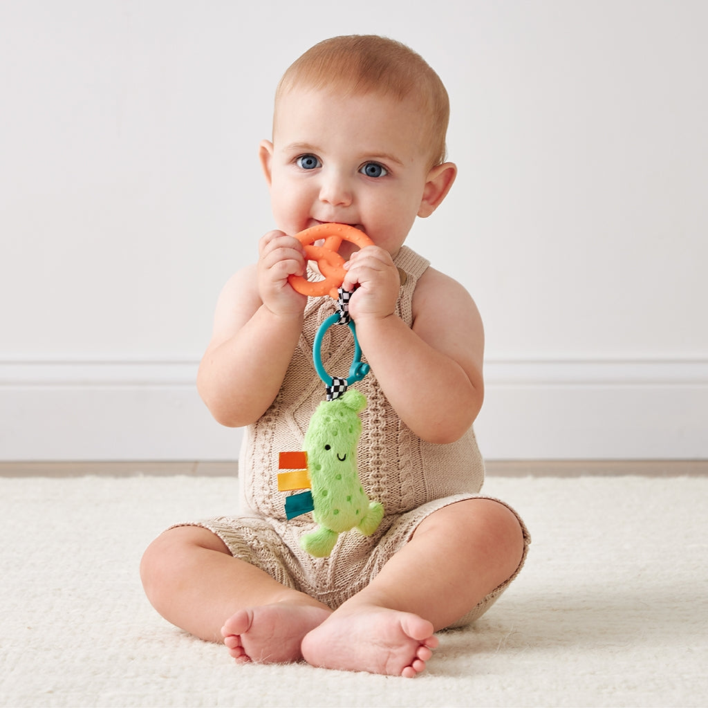 Baby sitting on a white floor holding a colorful teething toy.