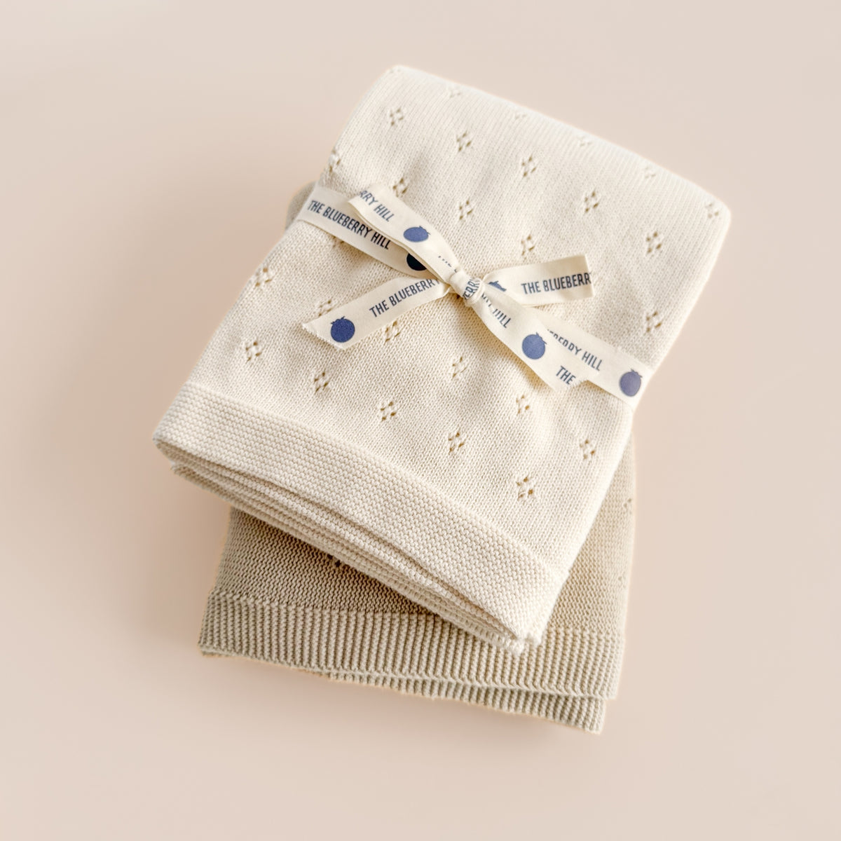 Two folded baby blankets with a brand label on a beige background